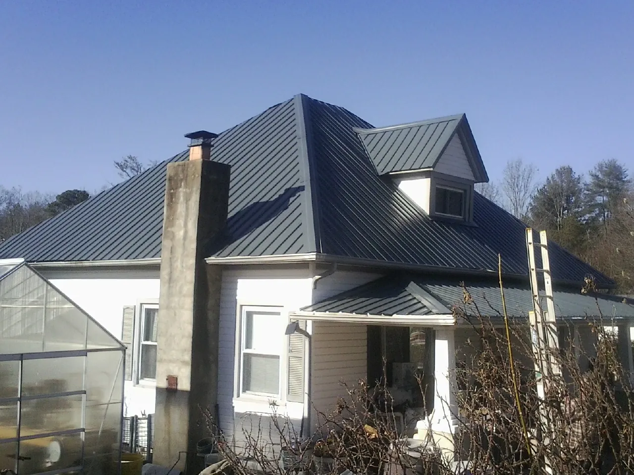 Dark blue standing seam metal roof on a white farmhouse with dormer — Slate & Tile Roof Repair by Roofing Brothers in Fremont