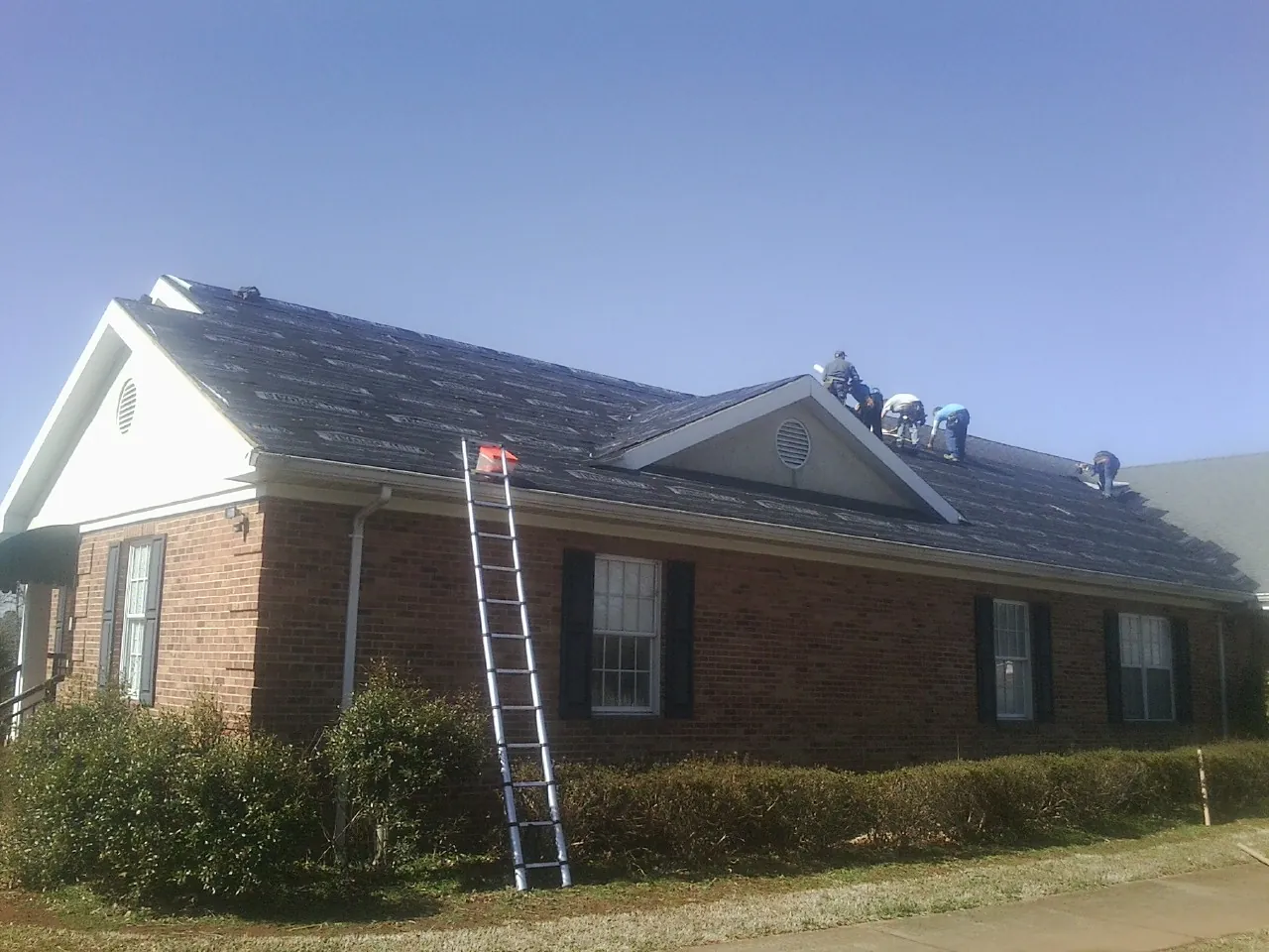 Crew tearing shingles off a brick ranch roof with a ladder set — Emergency Roof Repair work by our crew in Fremont