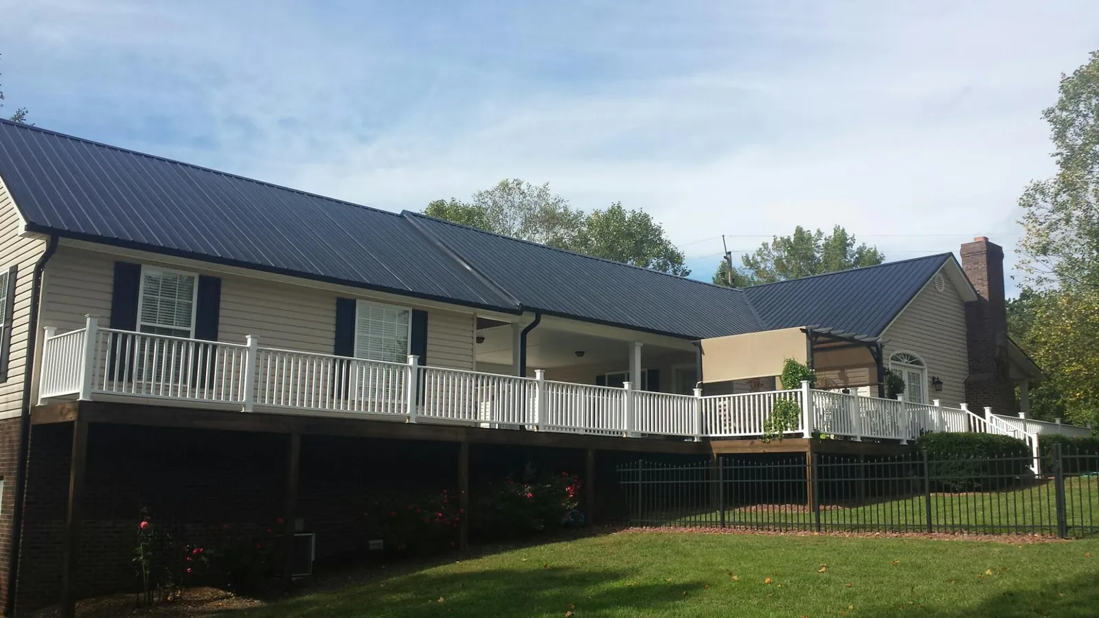 Black metal roof above a long white railed deck on a hillside home in Fremont